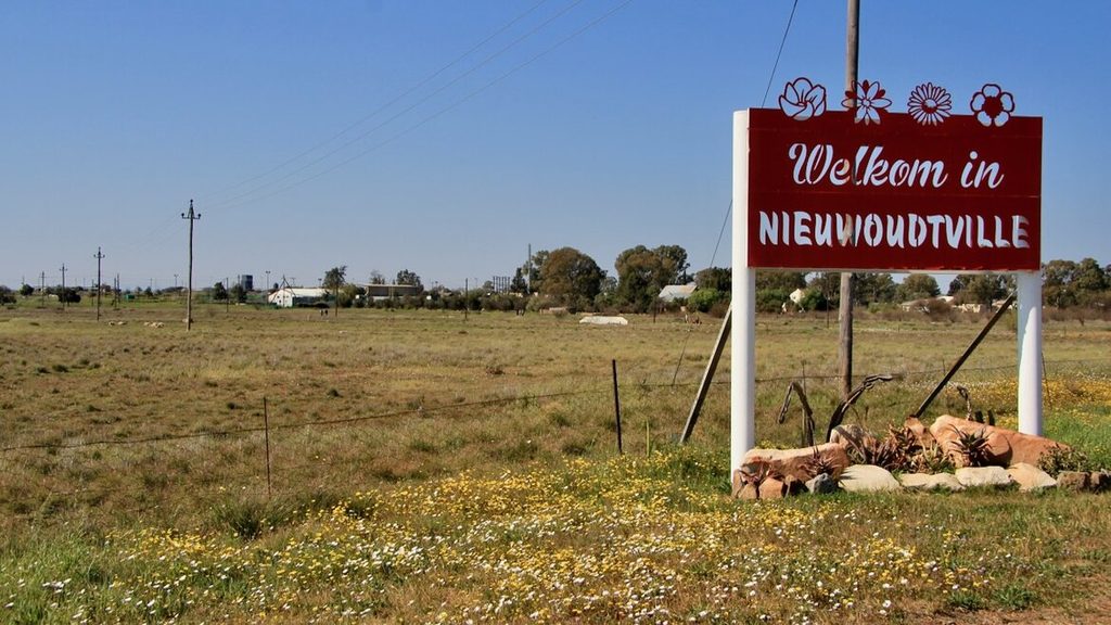 A welcome to Nieuwoudtville sign with yellow and white daisies at it's feet